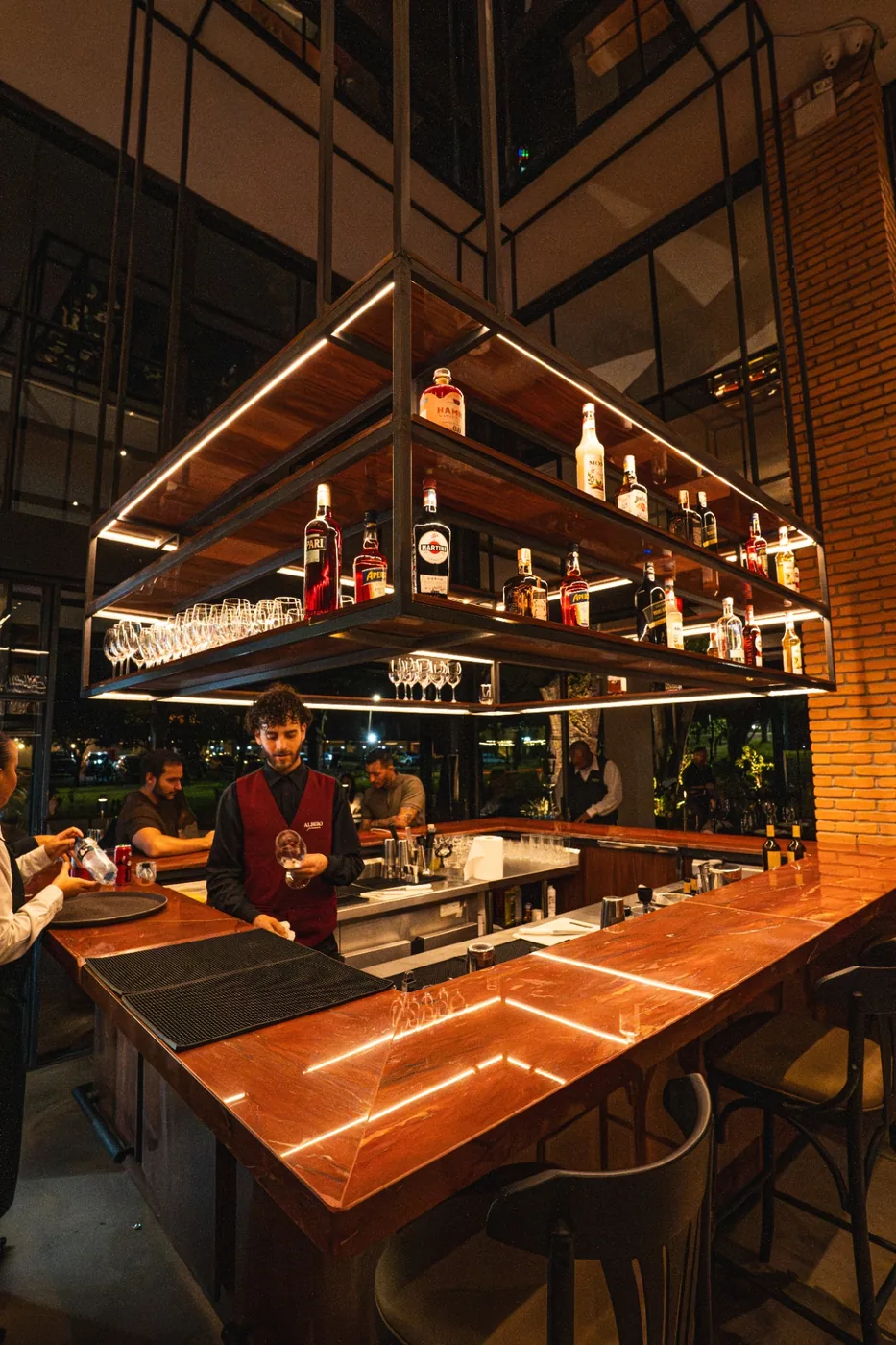 Bar em mármore vermelho com prateleiras retroiluminadas de destilados.