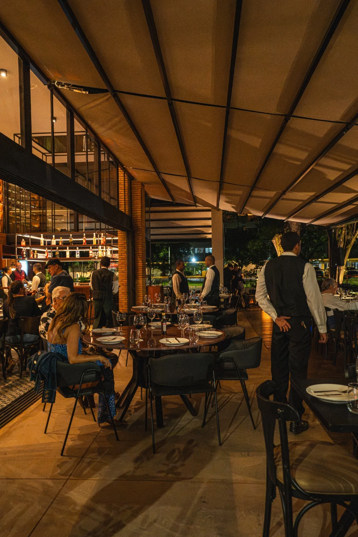 Salão coberto da Albero à noite, com mesas postas e brigada em serviço na 206 Sul.