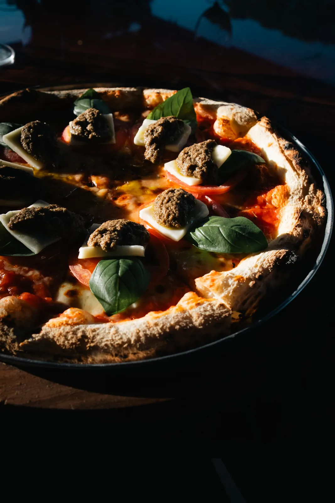 Pizza recém-saída do forno à lenha, com muçarela em fatias, pesto e manjericão fresco.
