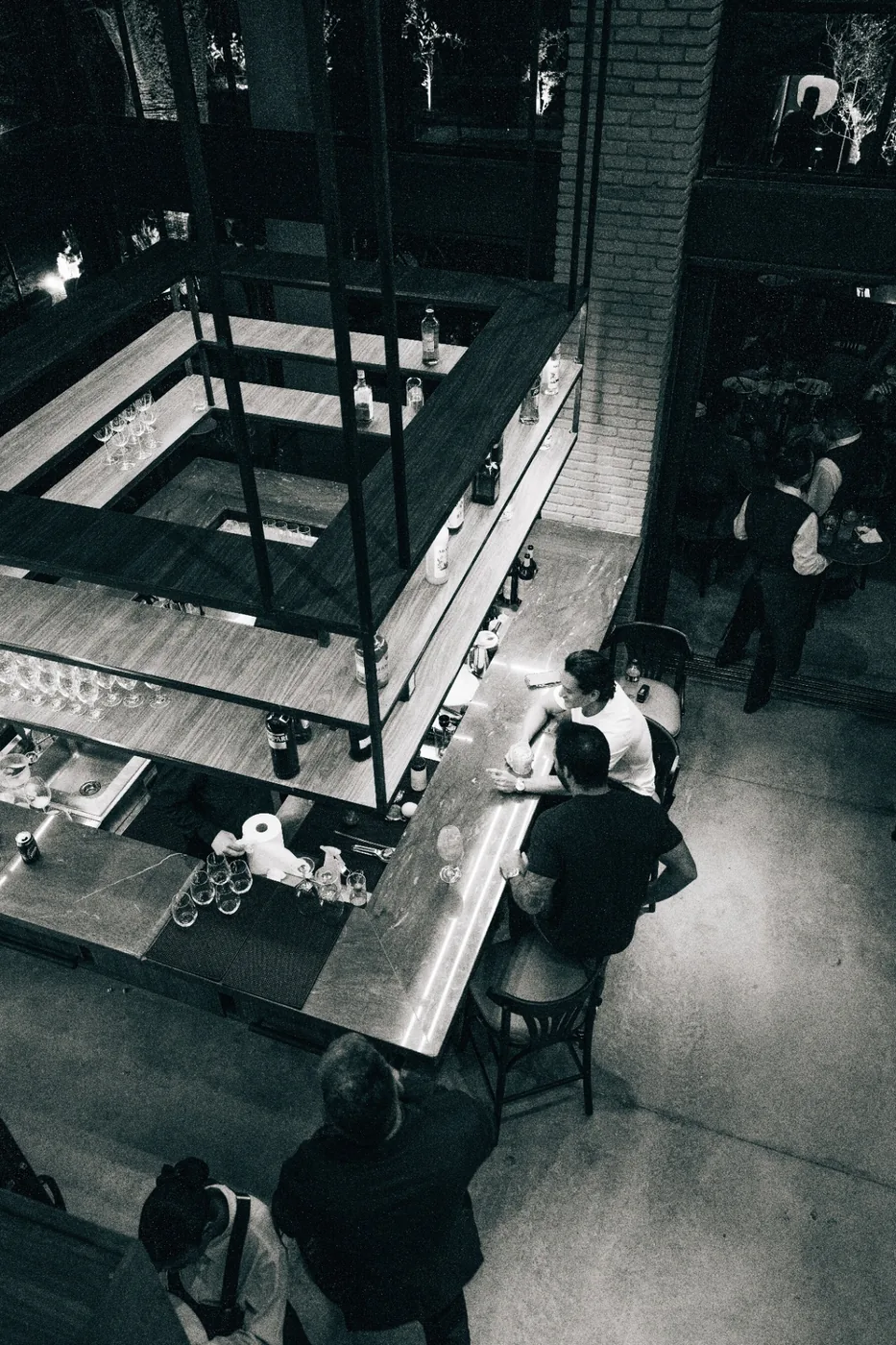 Vista aérea em preto e branco do bar circular com clientes em banquetas.